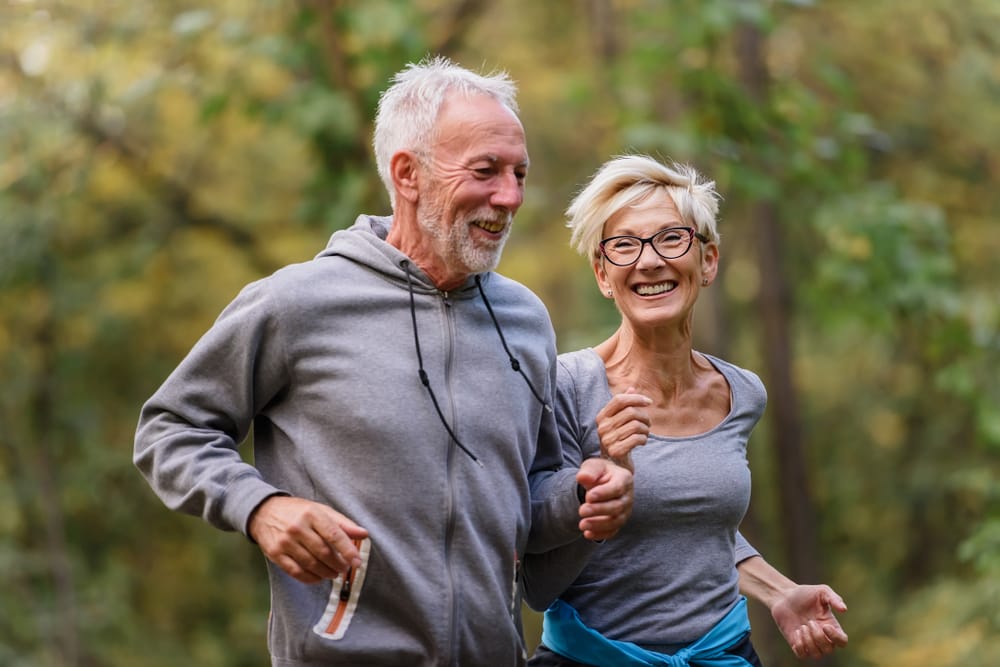 A happy senior couple enjoys jogging outdoors, promoting mobility, health, and energy at every age - Okolona Chiropractor.