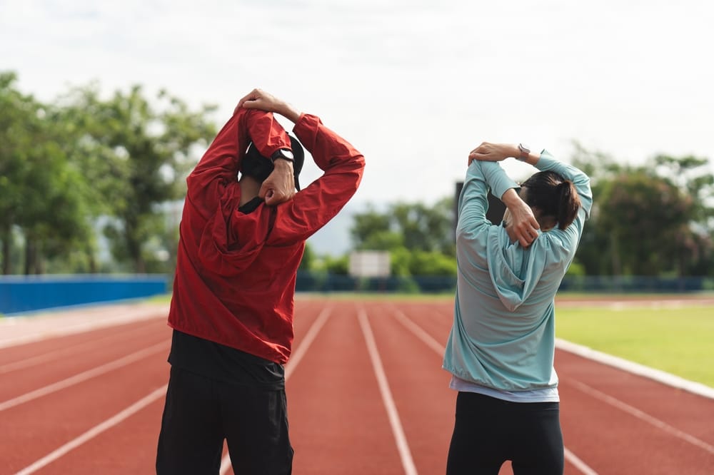 Two people stretch their arms on a running track, focusing on flexibility and preparation for exercise - Okolona Chiropractor.