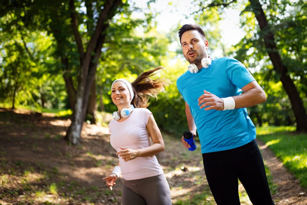A couple jogs through a scenic outdoor path, staying active and promoting healthy living - Chiropractor in Jeffersontown, KY.