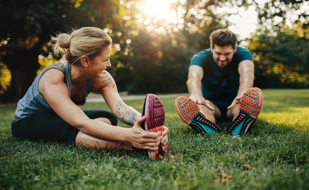 A man and woman enjoy outdoor partner stretching exercises to boost flexibility, health, and overall wellness - Chiropractor in Jeffersontown, KY.