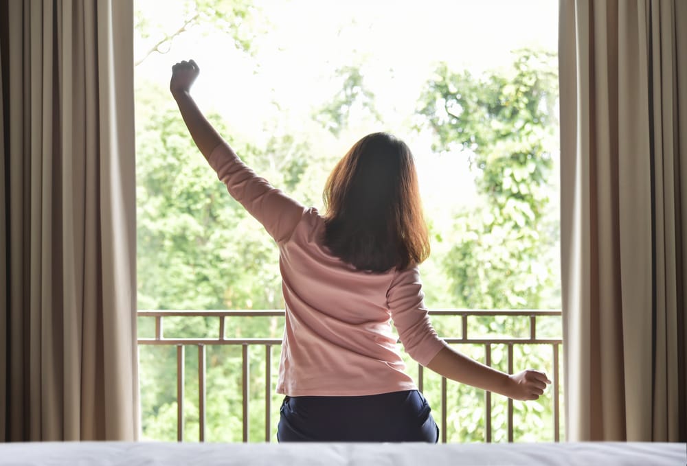A woman practices a refreshing morning stretch by the balcony to boost energy and improve posture - Chiropractor in St Matthews.