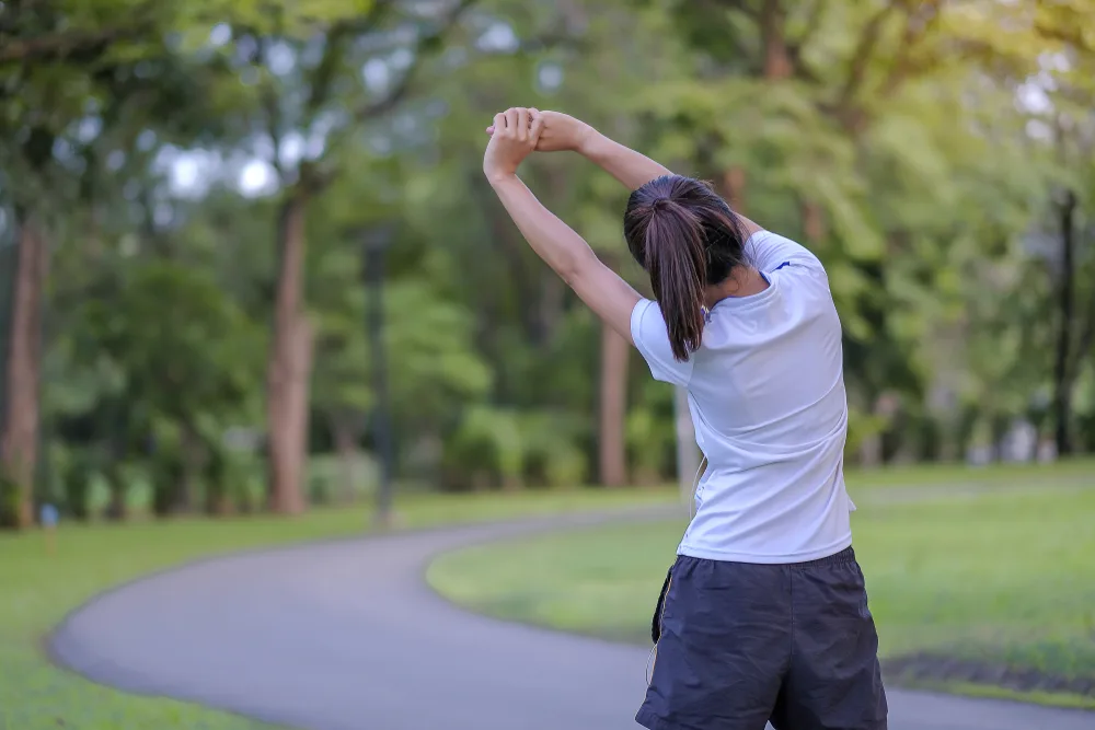 A person stretches outdoors to improve flexibility and back strength, supporting recovery and performance with Electro-Muscle Stimulation.